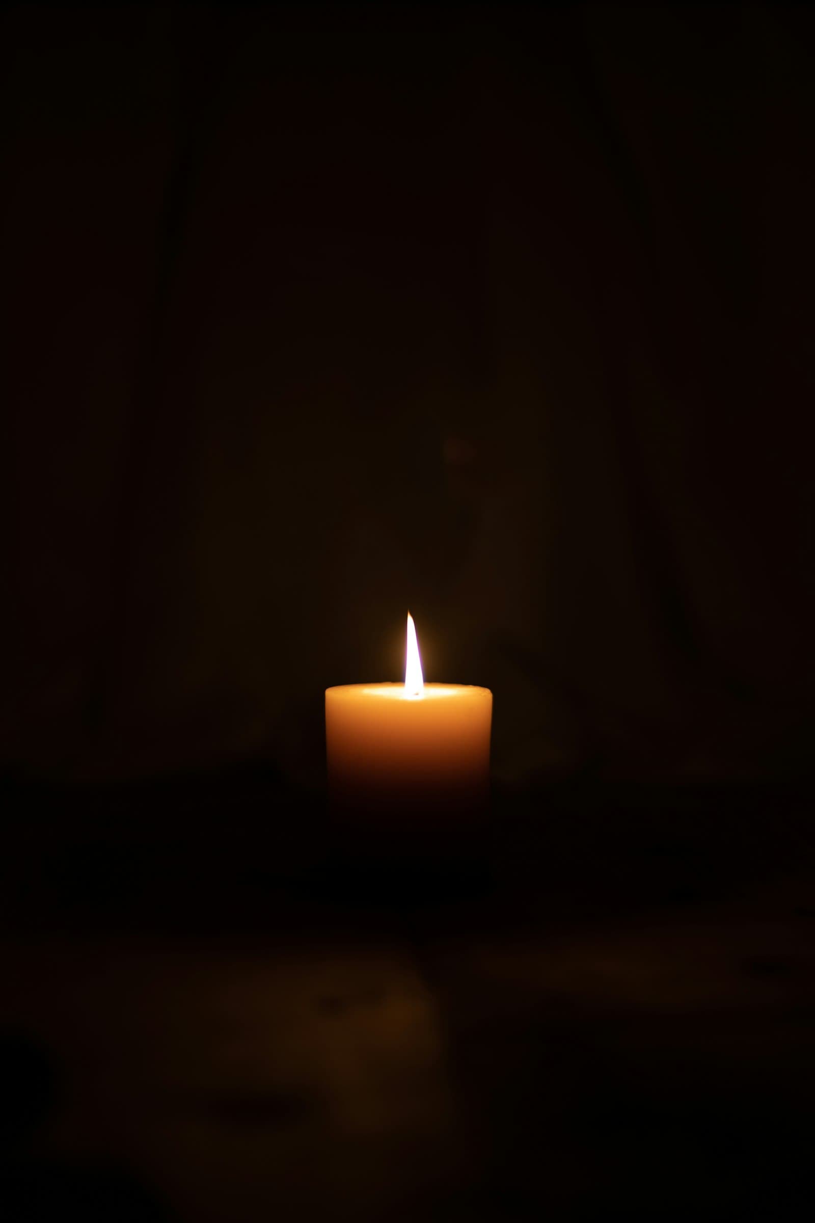 A single lit candle glowing in an otherwise completely dark room, quiet and intimate
