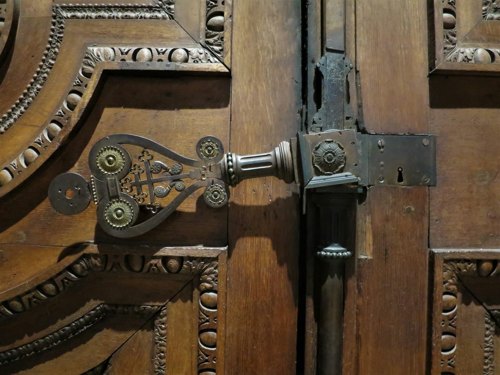 Close-up of an ornate antique brass door handle and lock plate on a carved wooden door