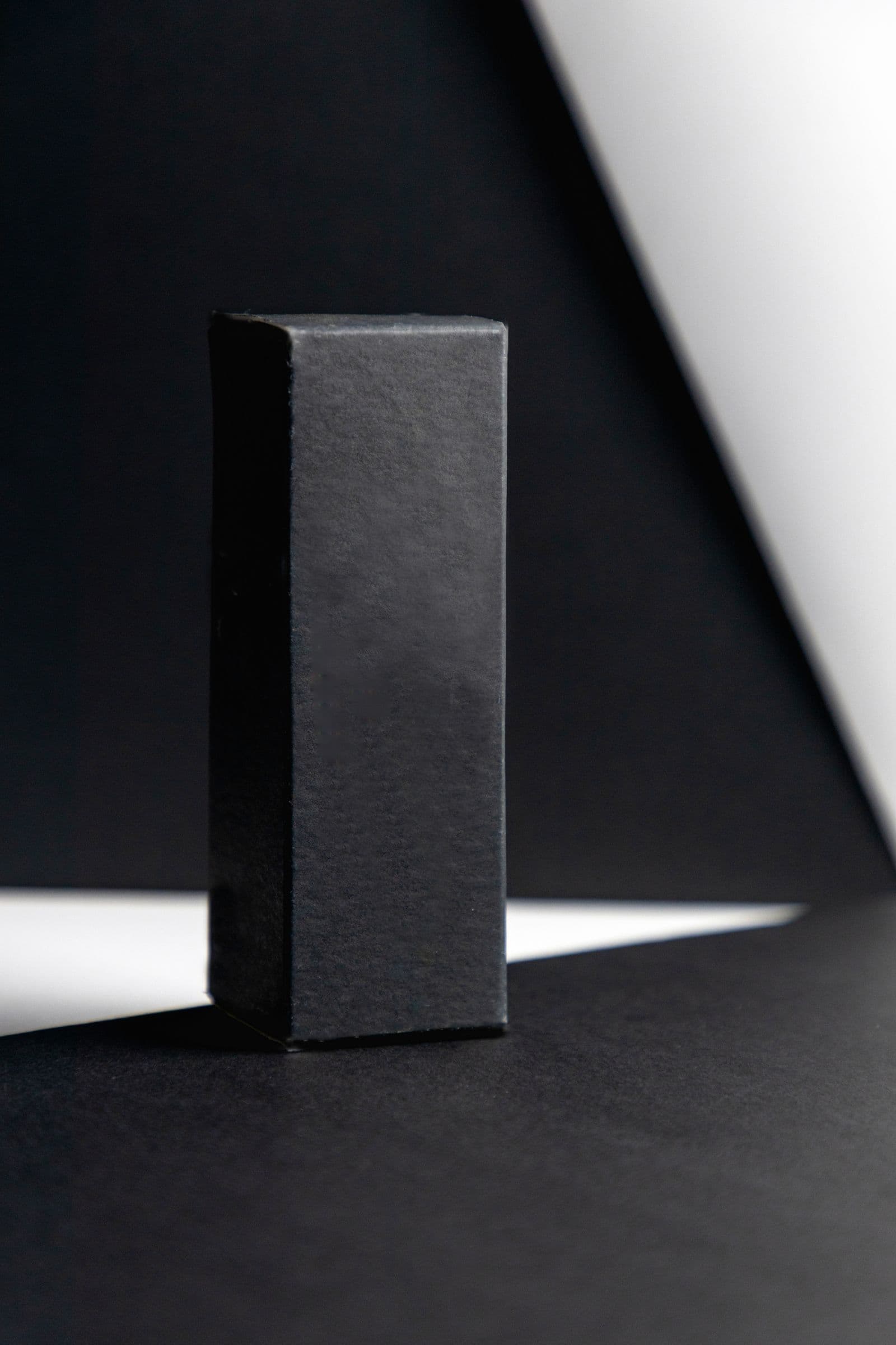 A minimalist black rectangular gift box against a dark background with a sharp diagonal shaft of light